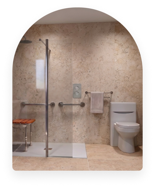 A level-access wet room with a fold-down seat, long-hose handset and grab rails, with space for a carer to assist.